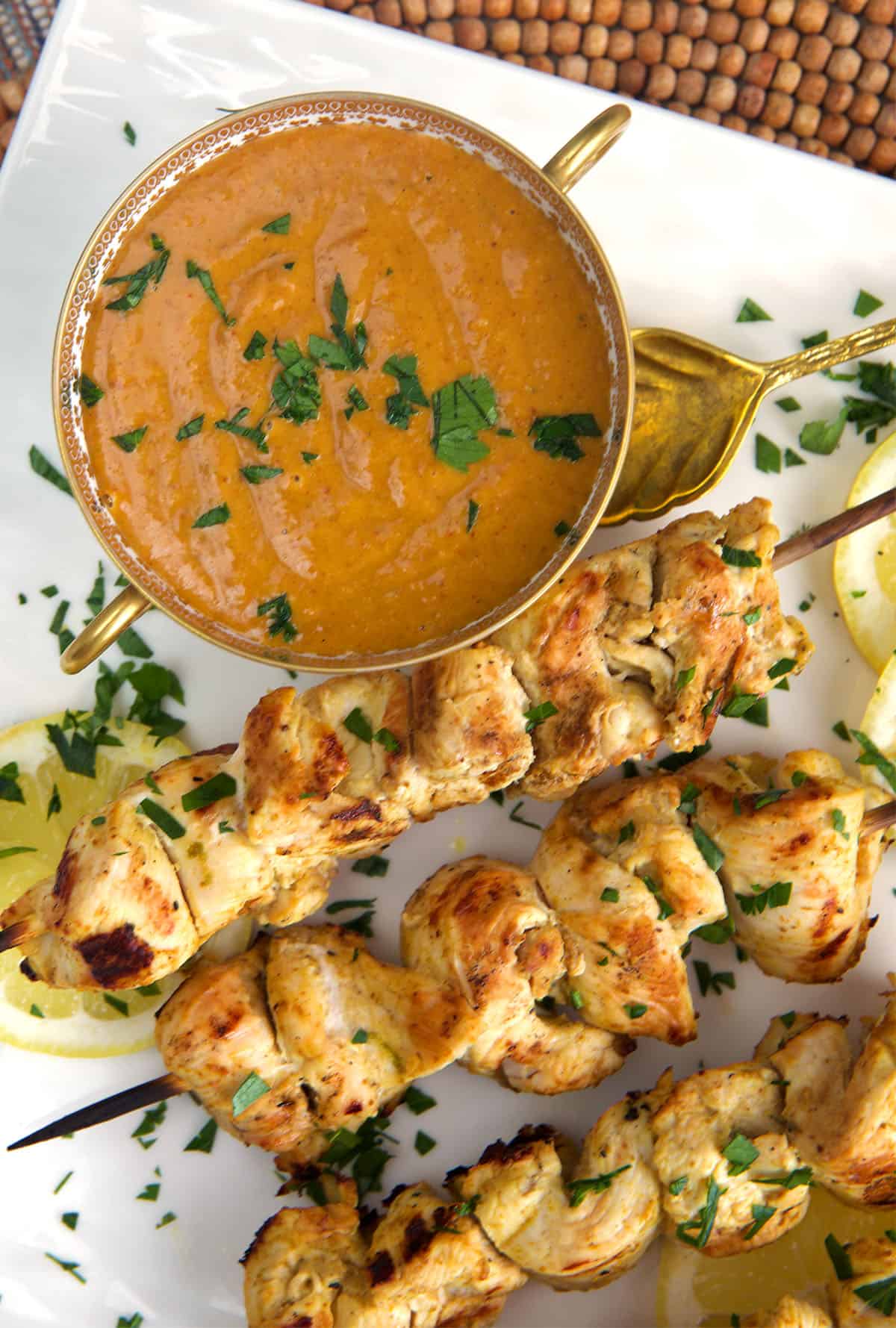 Chicken Satay on a platter with a bowl of peanut sauce.