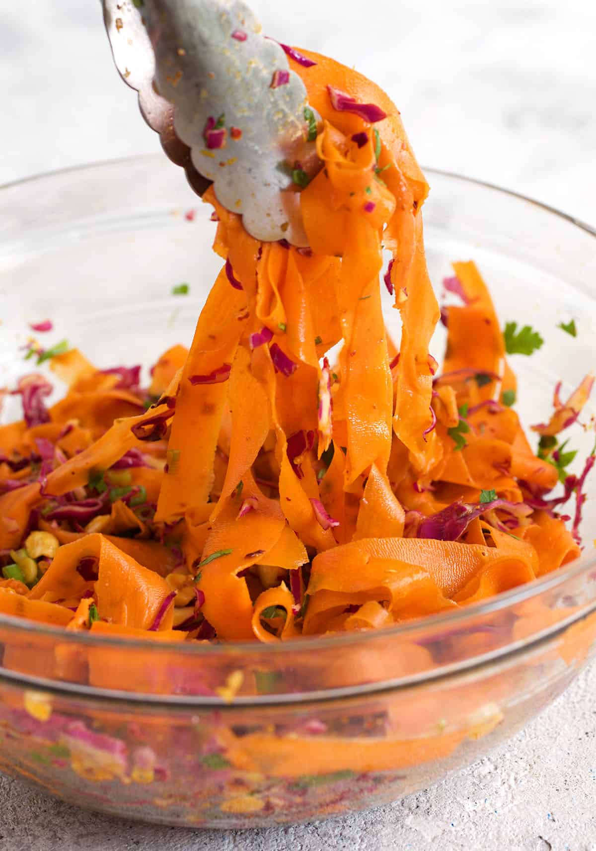 Carrot ribbon salad being tossed in a bowl with tongs.