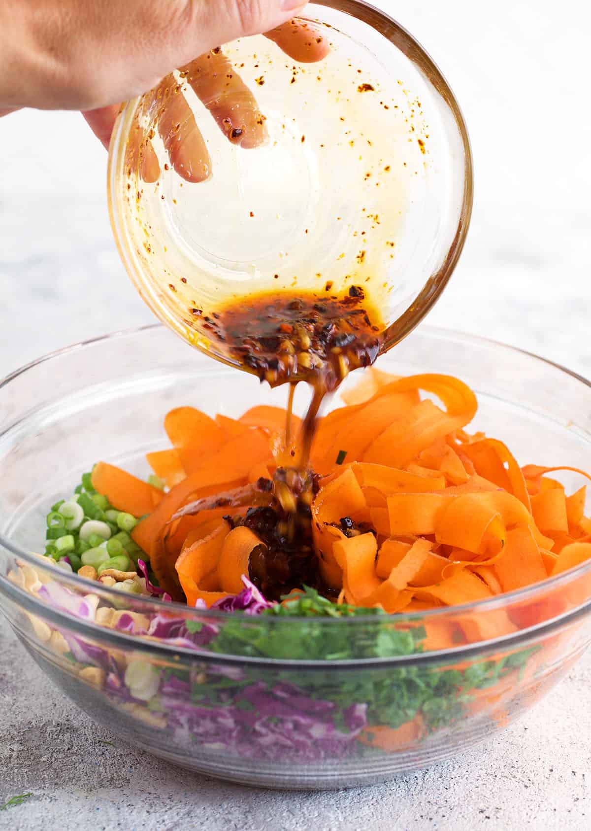 Dressing being poured over a bowl of carrot salad ingredients.