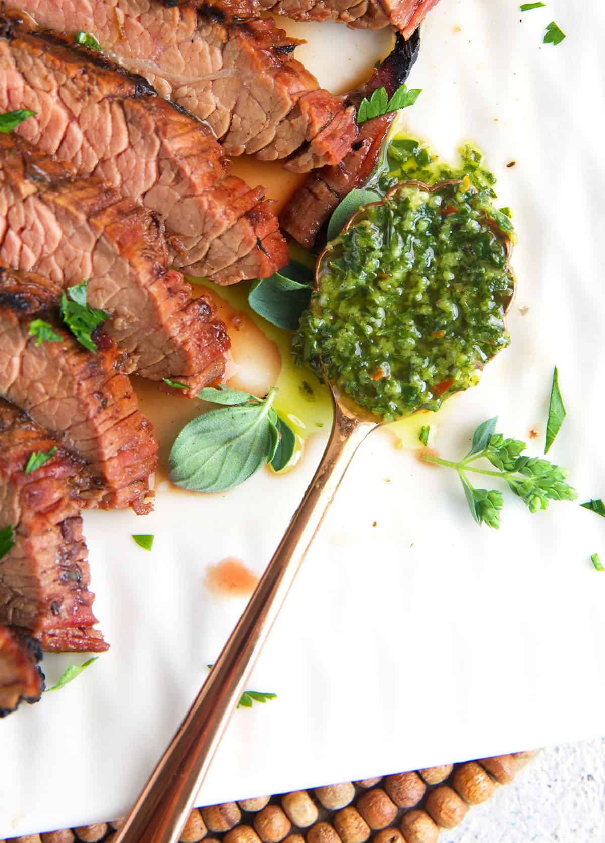 Chimichurri sauce on a spoon resting on a white platter with a sliced steak.