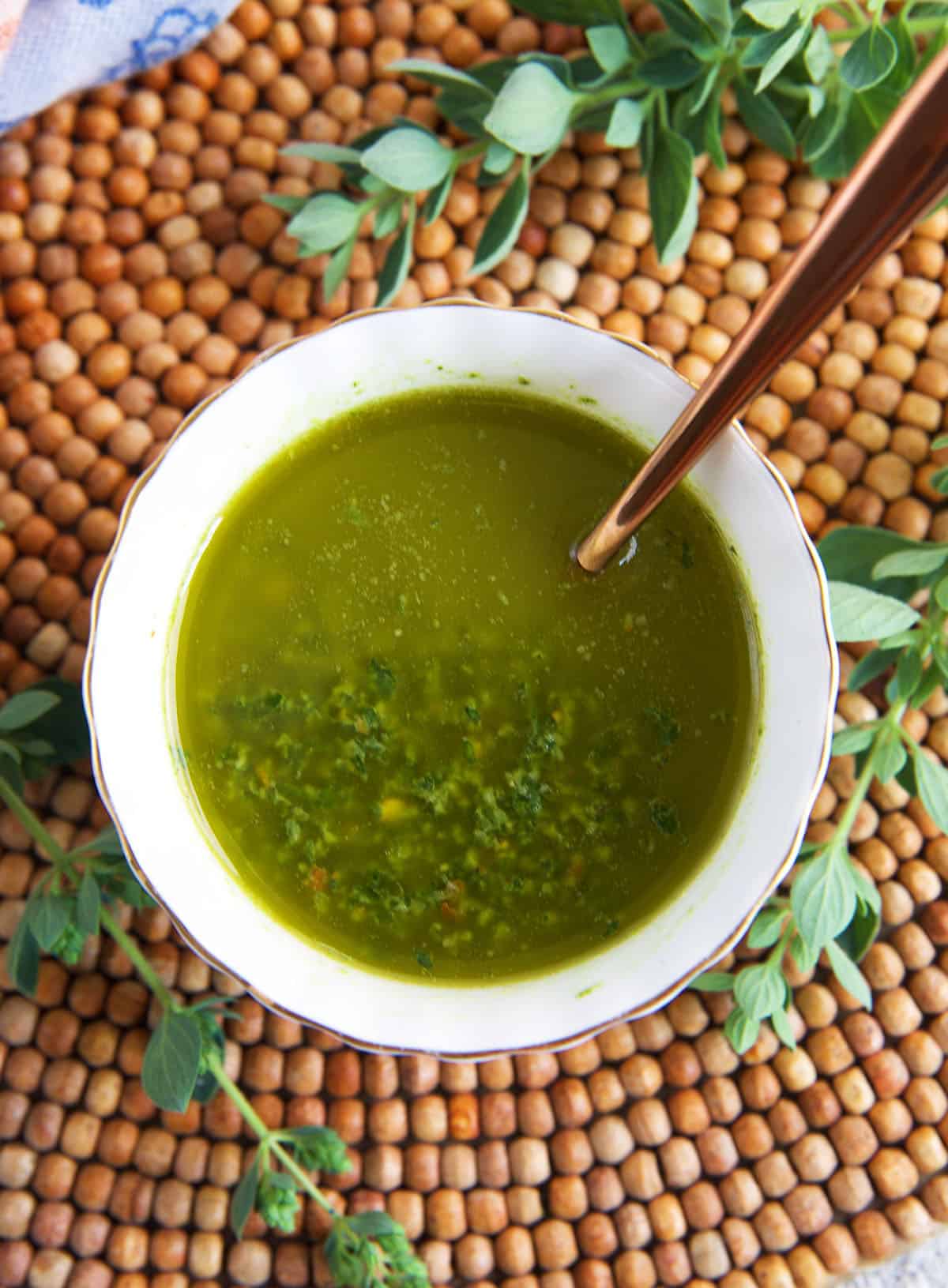 Chimichurri sauce in a white bowl with a copper spoon