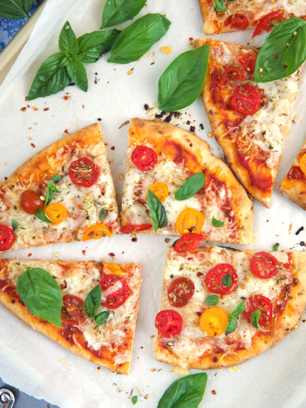 Flatbread pizza cut into quarters and topped with sliced tomatoes and basil.
