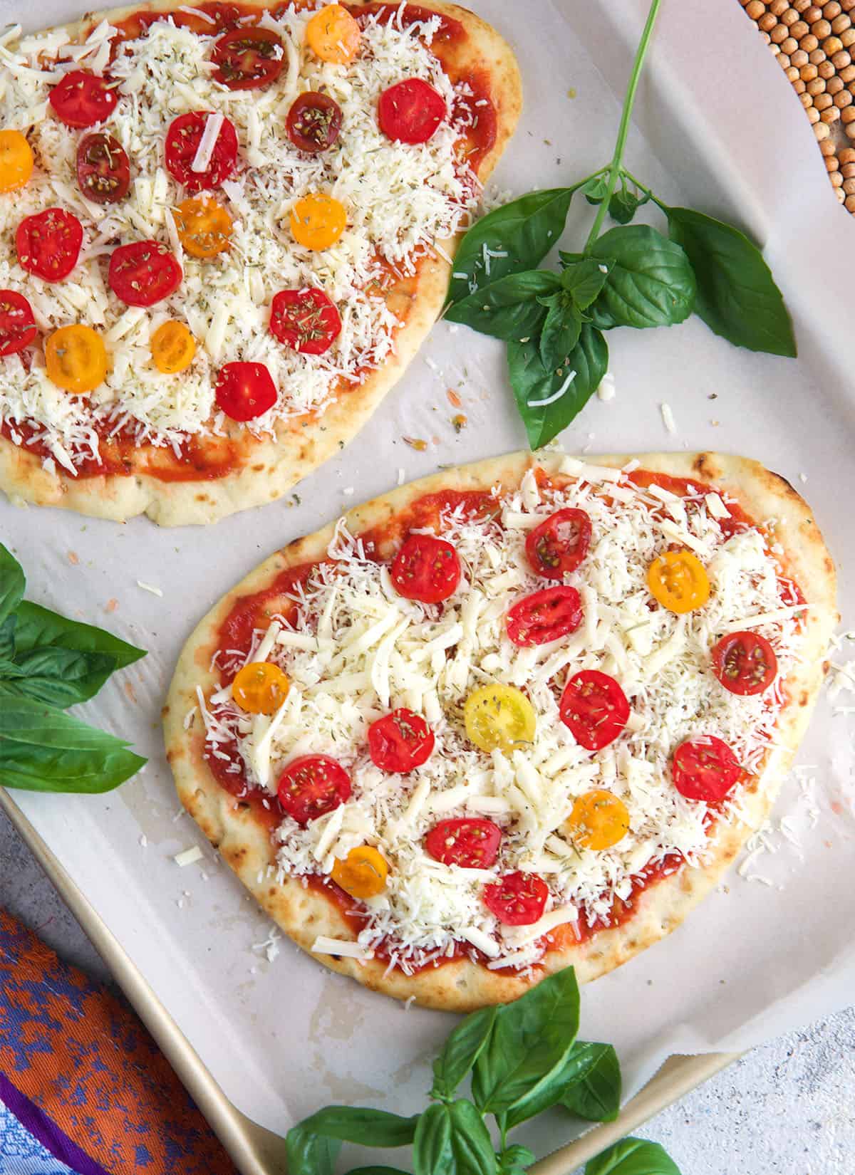 Flatbread pizzas on a baking sheet ready to go into the oven.