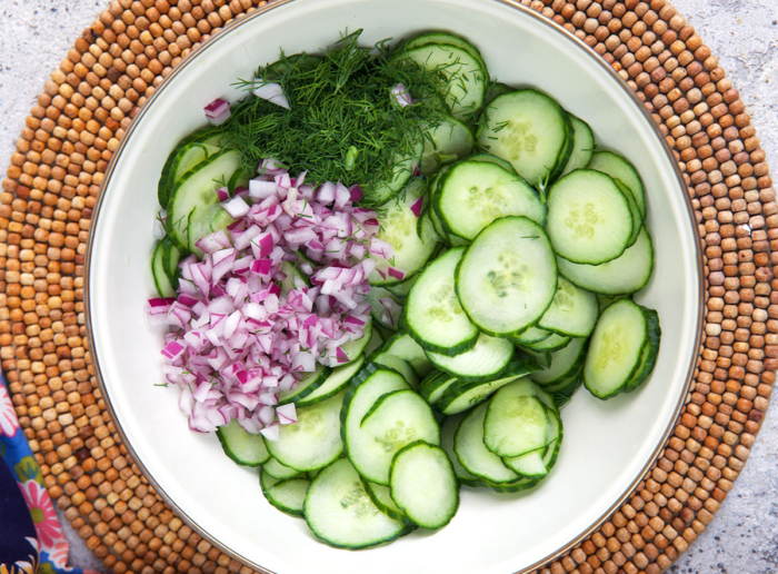 ingredients for cucumber salad prepared and ready to be tossed with dressing in a white mixing bowl