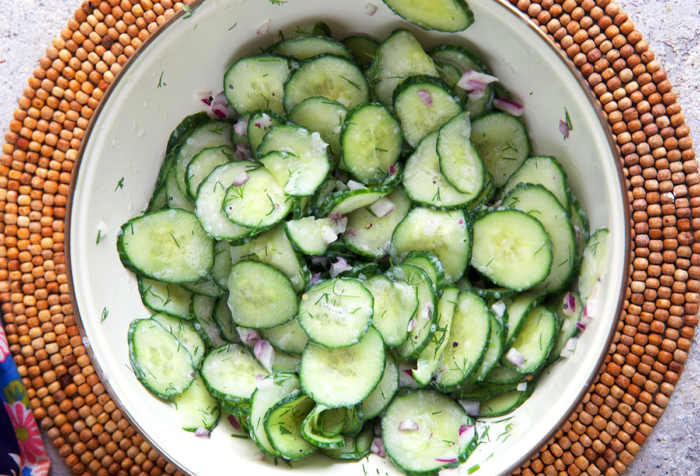 Cucumber salad tossed with dressing in a white mixing bowl