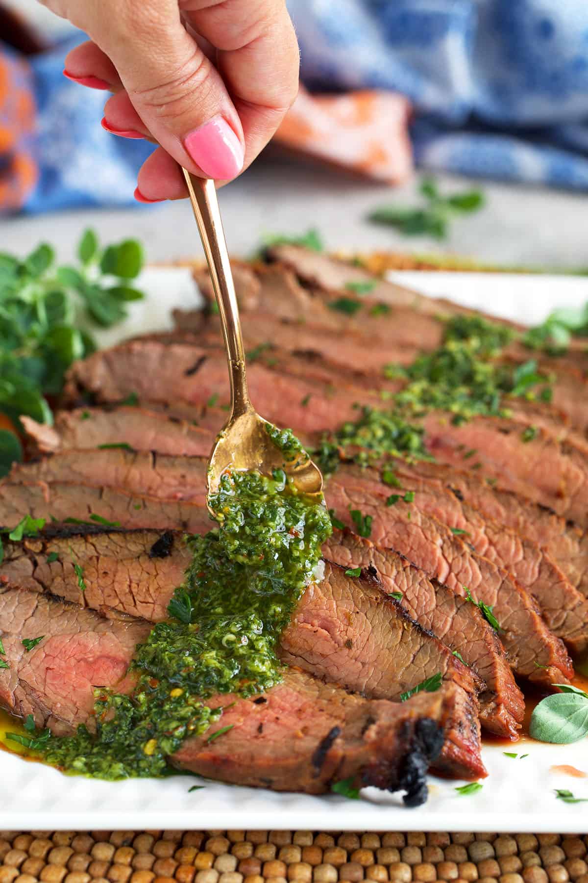 Chimichurri sauce being spooned over a grilled flank steak plated on a white platter.