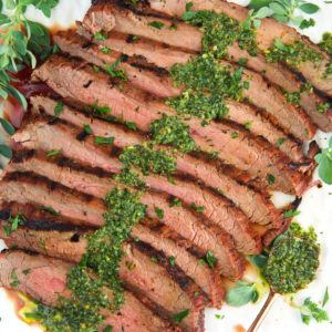 Grilled flank steak with chimichurri sauce on top plated on a white platter