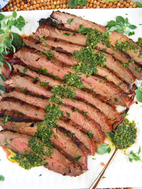 Grilled flank steak with chimichurri sauce on top plated on a white platter