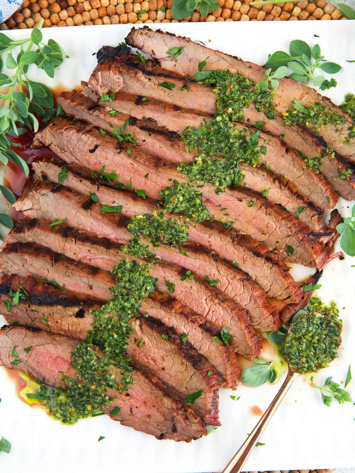 Grilled flank steak with chimichurri sauce on top plated on a white platter