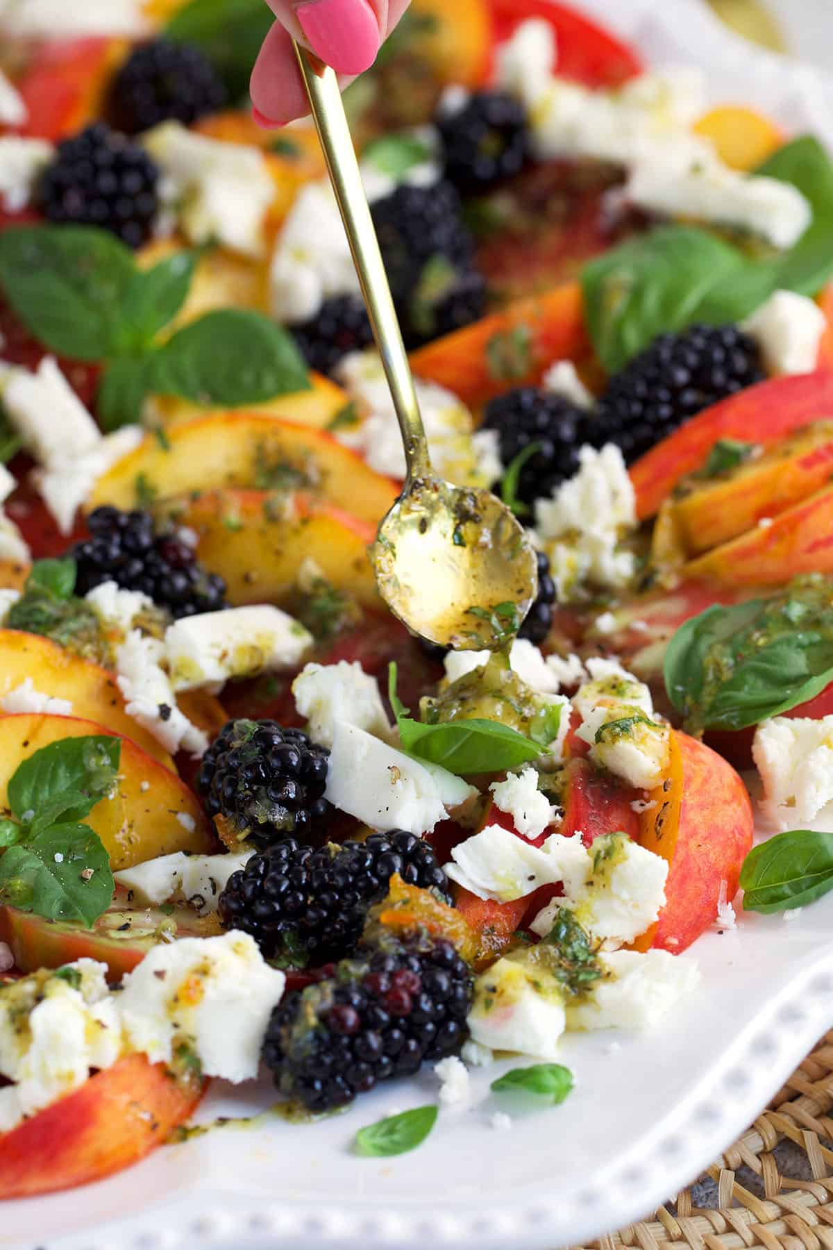 Dressing being drizzled on a Peach Caprese Salad with a gold spoon.