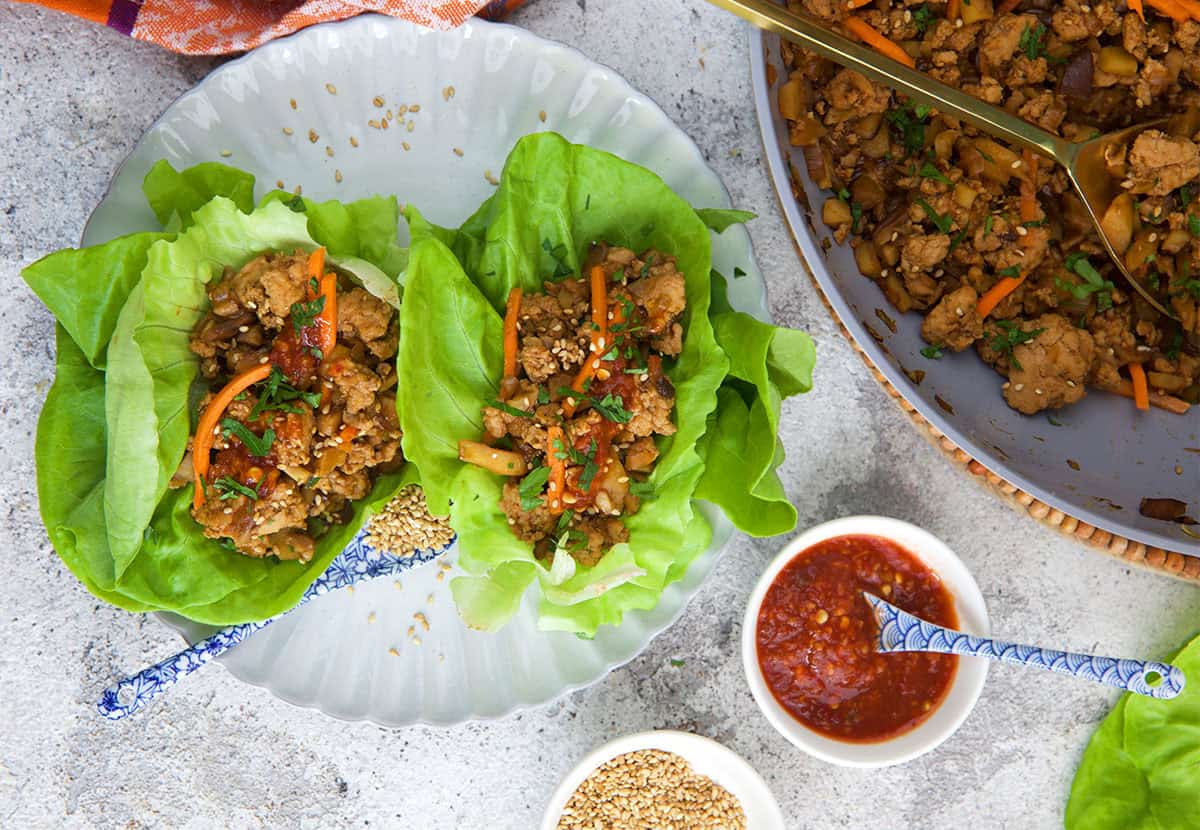 two chicken lettuce wraps on a white plate with two dishes of sauce