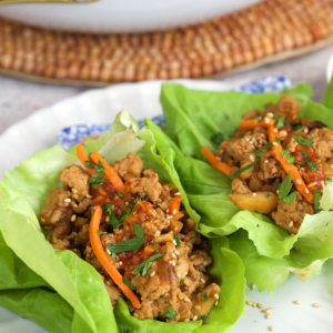 chicken lettuce wraps on a white plate and topped with sauce and carrots