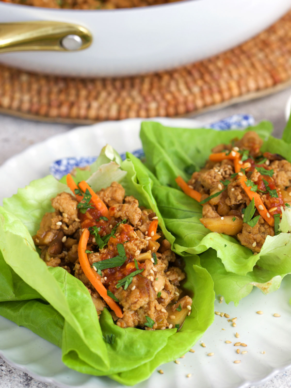 chicken lettuce wraps on a white plate and topped with sauce and carrots