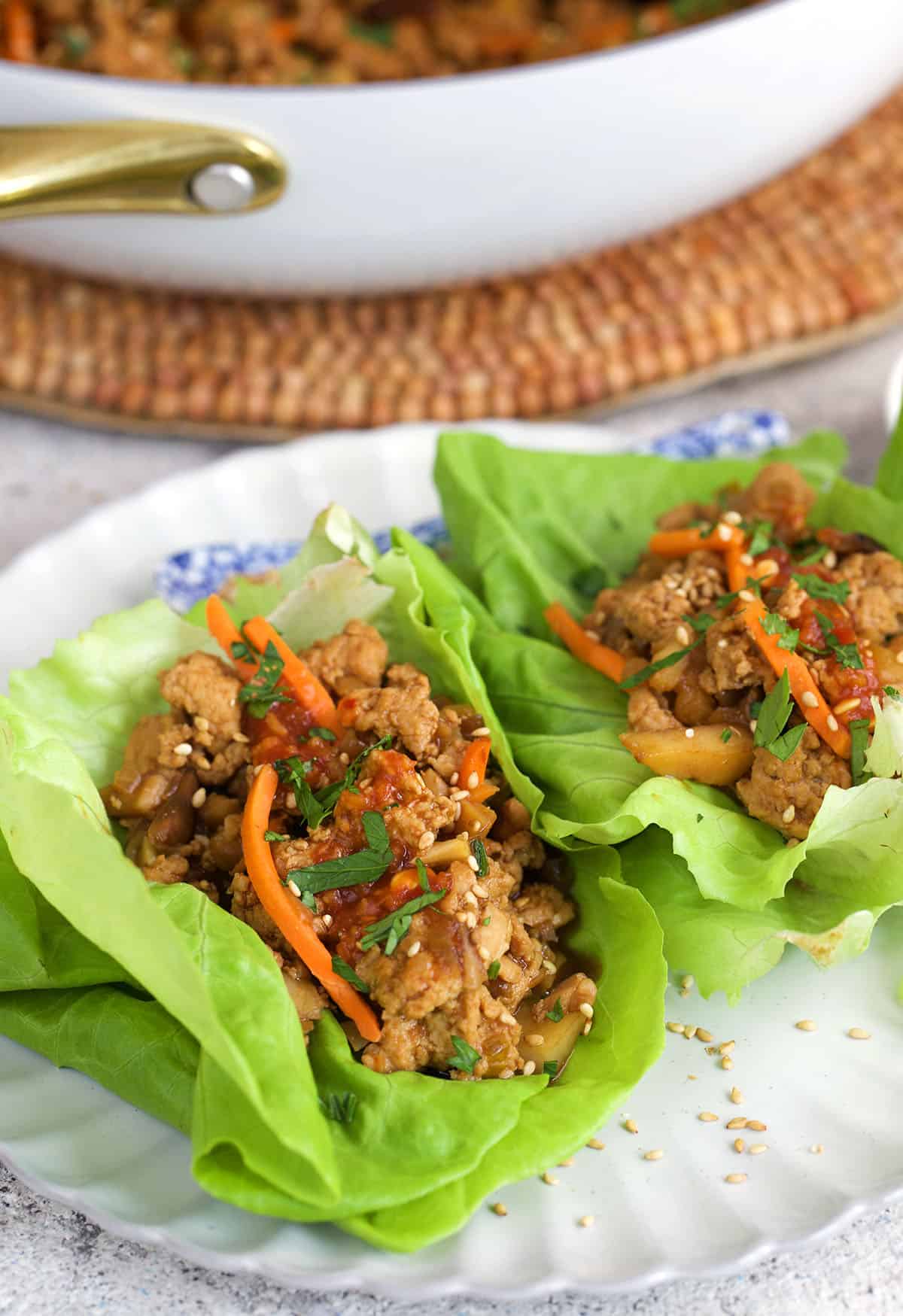 chicken lettuce wraps on a white plate and topped with sauce and carrots