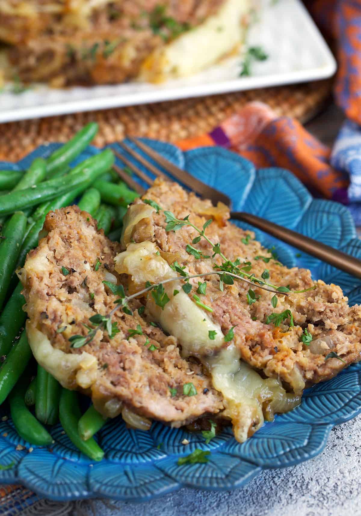 French onion meatloaf sliced on a blue plate with green beans.
