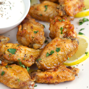 Lemon Pepper Wings on a white platter with lemon slices and a white dipping sauce.