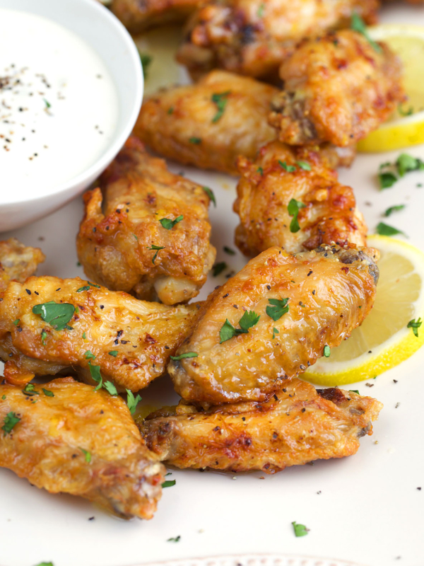 Lemon Pepper Wings on a white platter with lemon slices and a white dipping sauce.