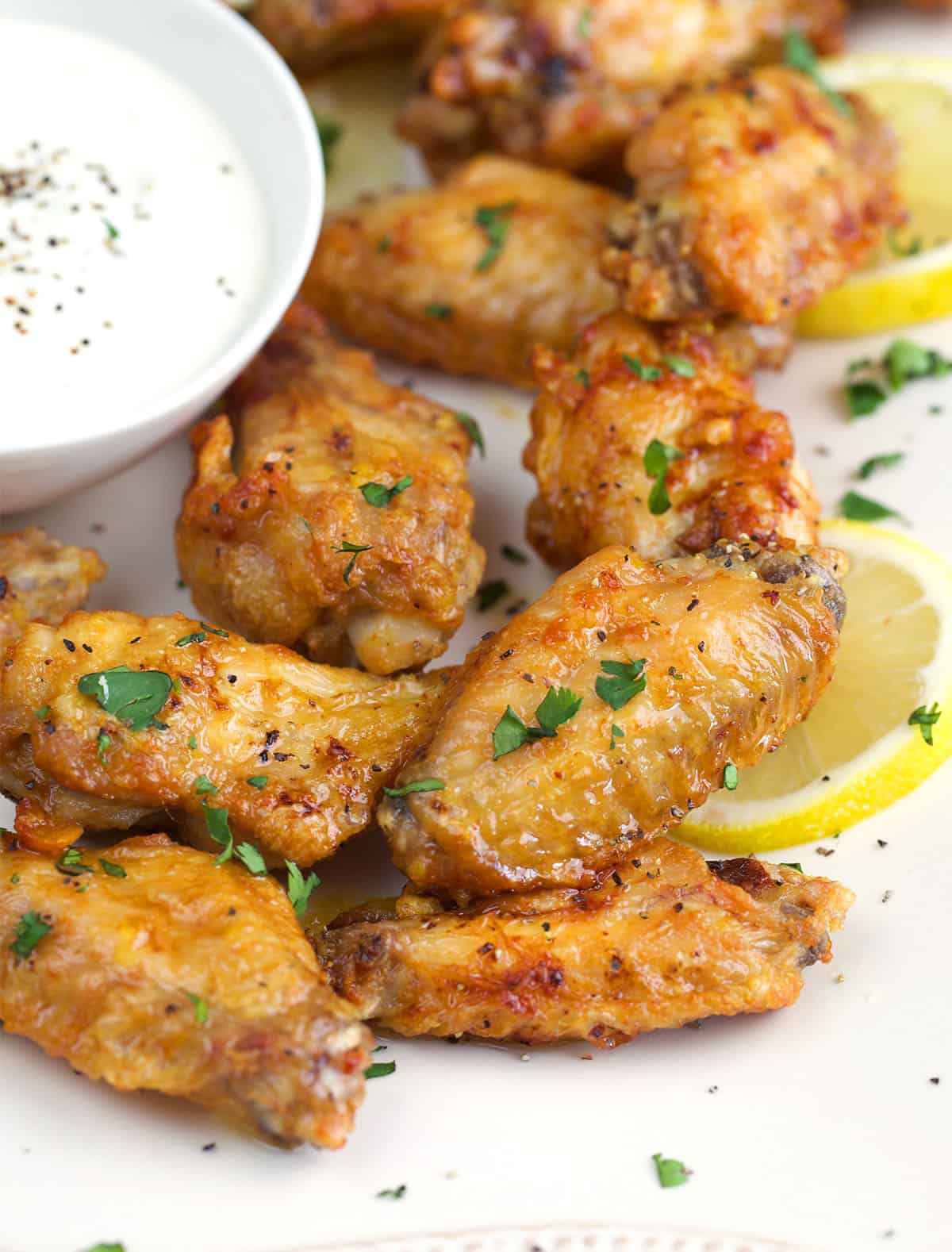 Lemon Pepper Wings on a white platter with lemon slices and a white dipping sauce.