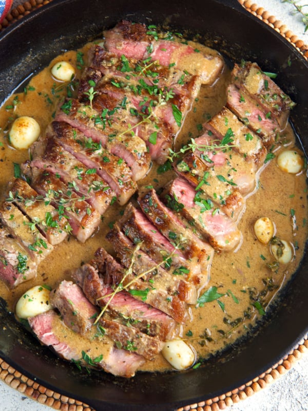 NY Strip Steak sliced and served in a cast iron skillet with creamy pan sauce