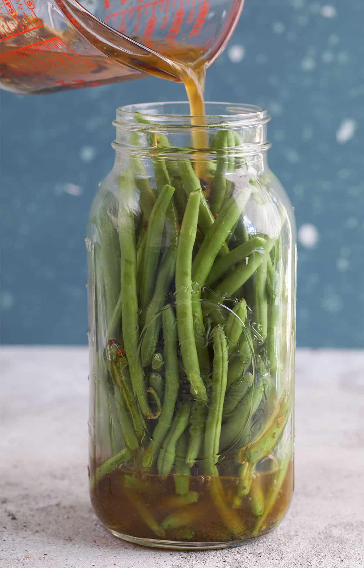 Green beans in a glass jar with pickle brine being poured over top