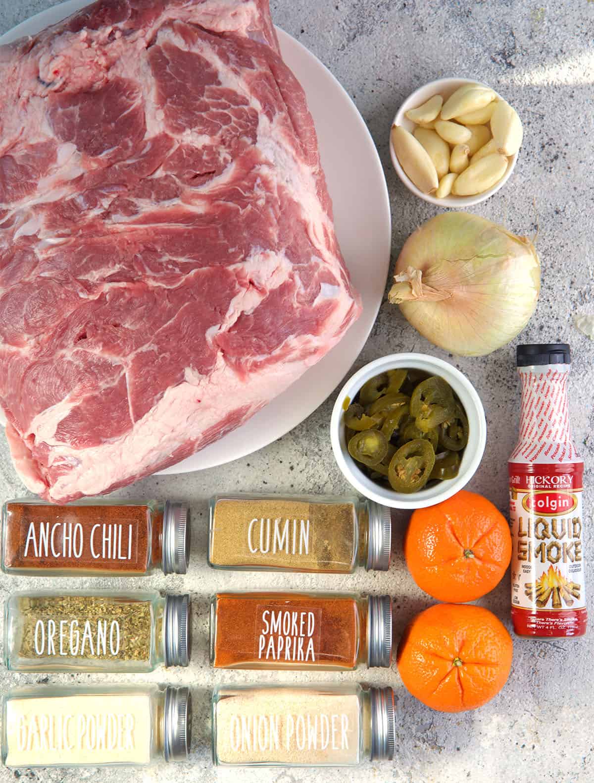 Ingredients for pork carnitas including pork roast, spices, jalapeños, oranges, liquid smoke and onion.