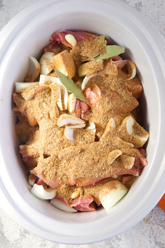 Pork roast in a slow cooker with spices, onions and jalapeños ready to be cooked