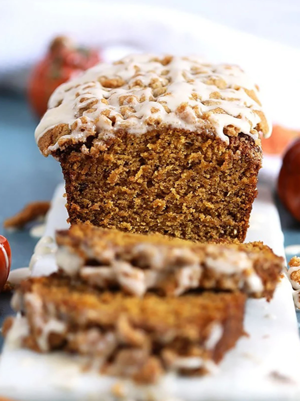 Pumpkin Banana Bread with glaze on a streusel topping and two slices stacked in front.