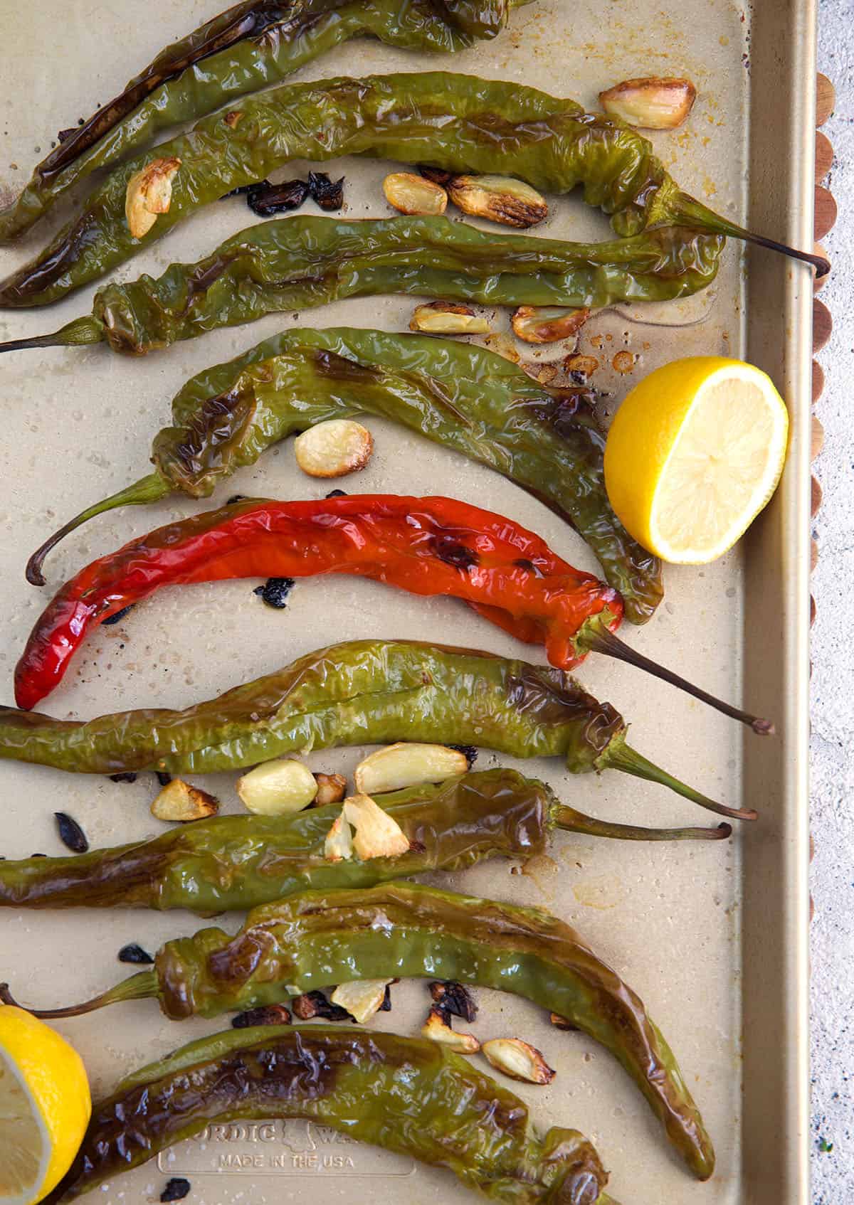 Roasted Long Hot peppers with garlic on a baking sheet with two lemon halves.