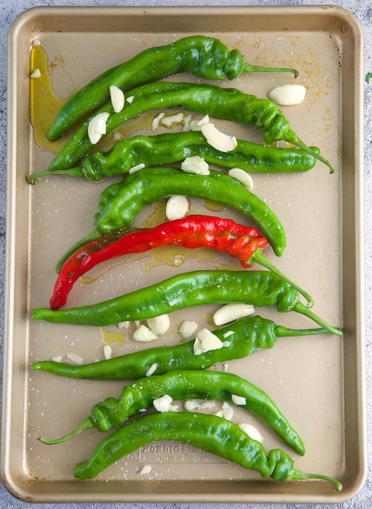 Long hot peppers on a baking sheet with garlic cloves