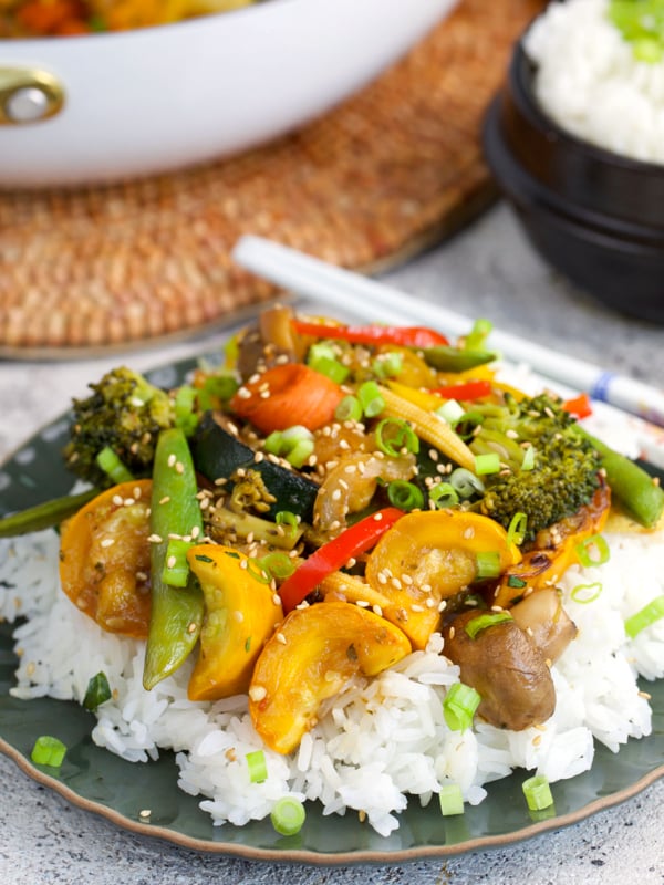Stir Fried Vegetables on a bed of rice plates on a green plate with white chopsticks.