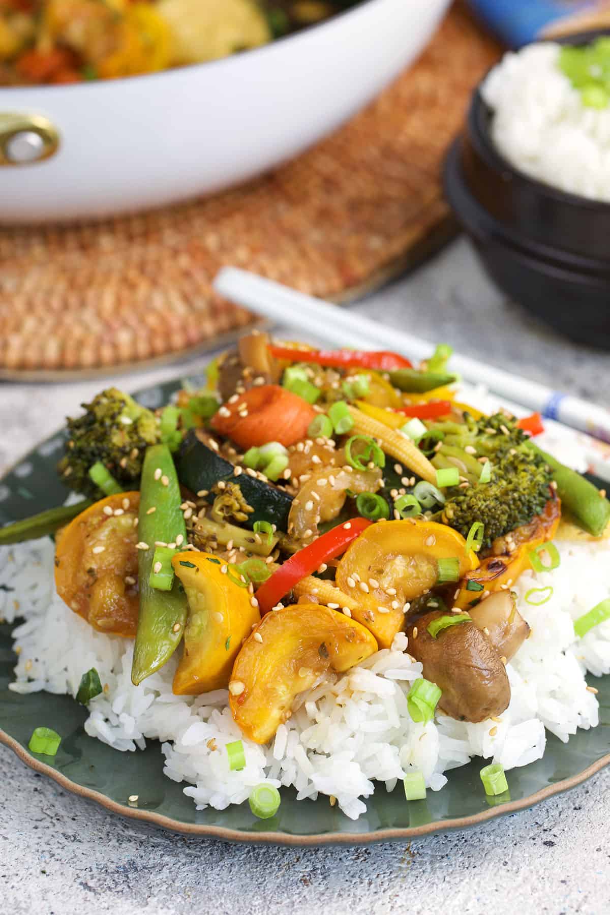 Stir Fried Vegetables on a bed of rice plates on a green plate with white chopsticks.