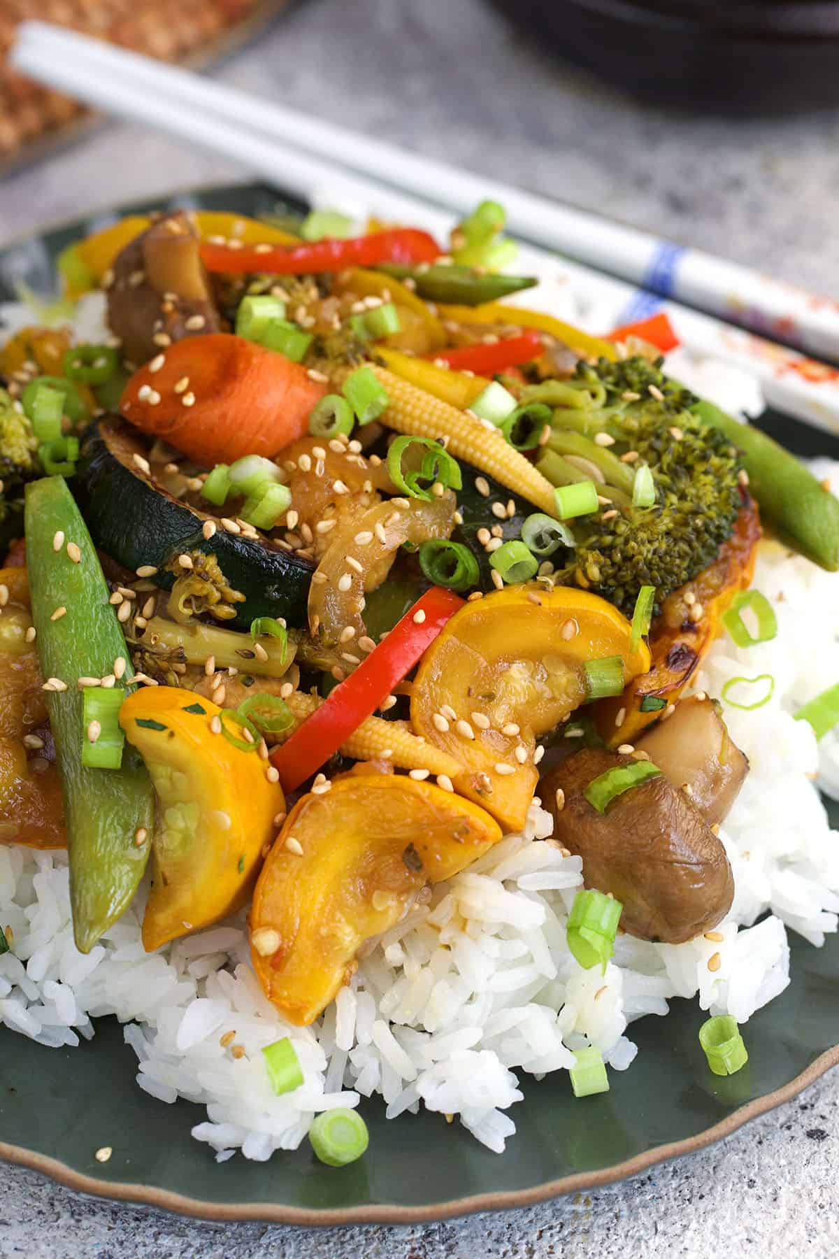 vegetable stir fry on white rice with white chopsticks next to it