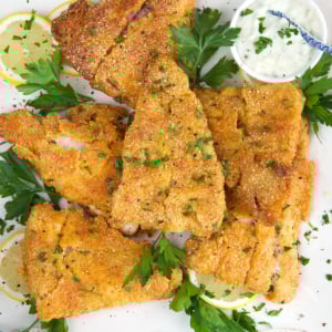 Fried Catfish fillets on a white platter with parsley and tartar sauce.