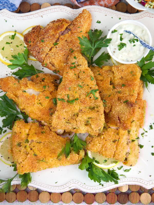 Fried Catfish fillets on a white platter with parsley and tartar sauce.