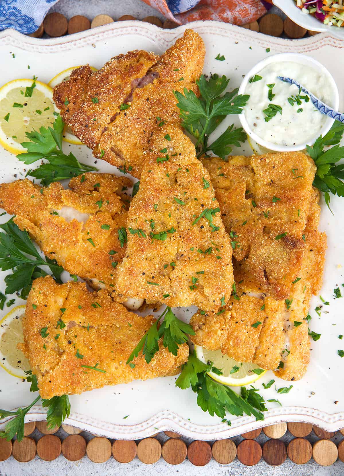 Fried Catfish fillets on a white platter with parsley and tartar sauce.