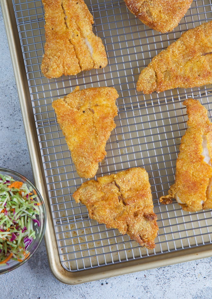 golden fried catfish on a baking sheet with wire rack after frying.