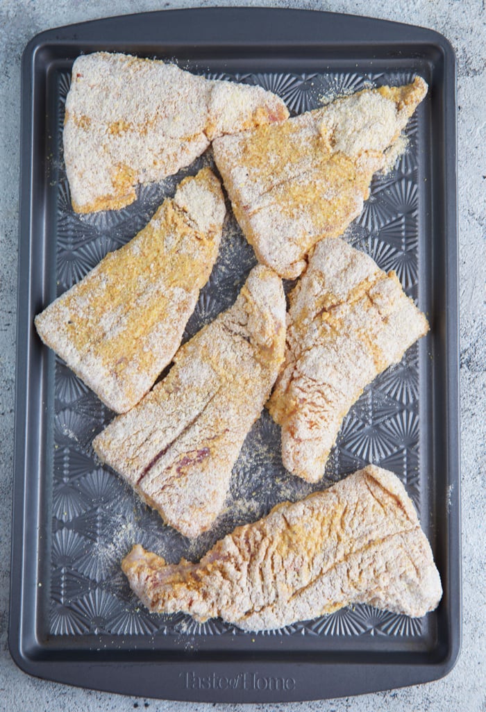 dredged catfish fillets on a baking sheet