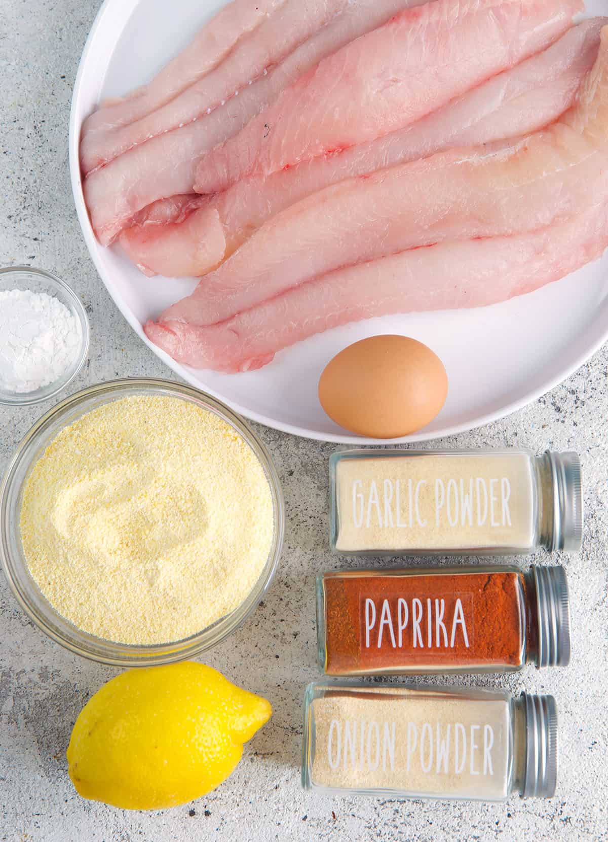 Ingredients for Southern fried Catfish, catfish filets on white plate, cornmeal, spices and lemon