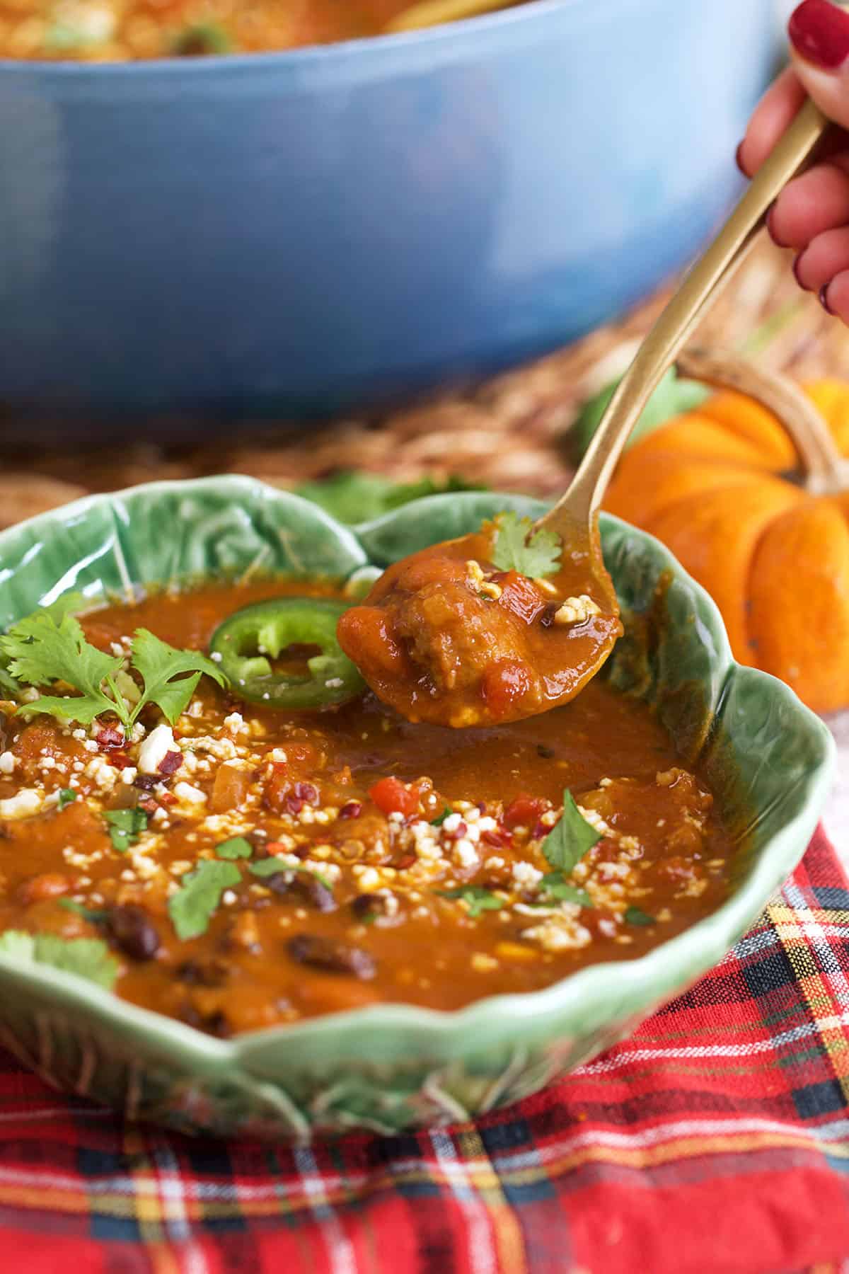 Pumpkin Chili in a cabbage leaf bowl with a gold spoon scooping up a serving.