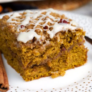 slice of pumpkin coffee cake on a white plate with a cinnamon stick