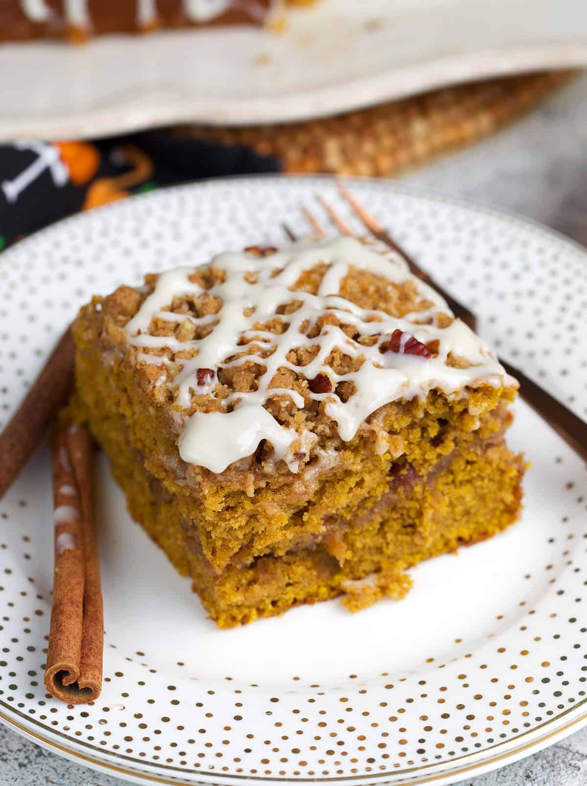 Pumpkin Coffee Cake square on a plate with two cinnamon sticks and a fork.