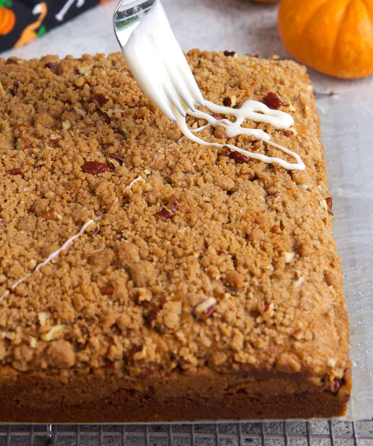 Fork drizzling glaze over pumpkin coffee cake.