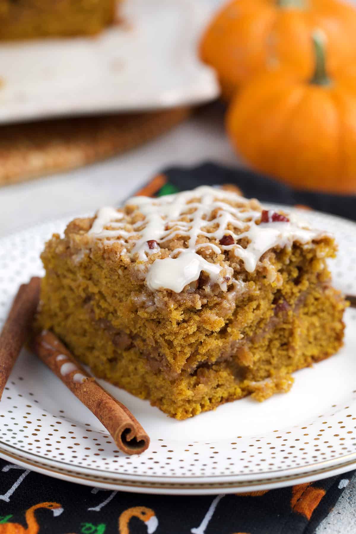 Pumpkin crumb Cake slice on a white plate with cinnamon sticks and a couple mini pumpkins in the background