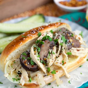 Chicken Cheesesteak Sandwich on a white plate topped with mushrooms.