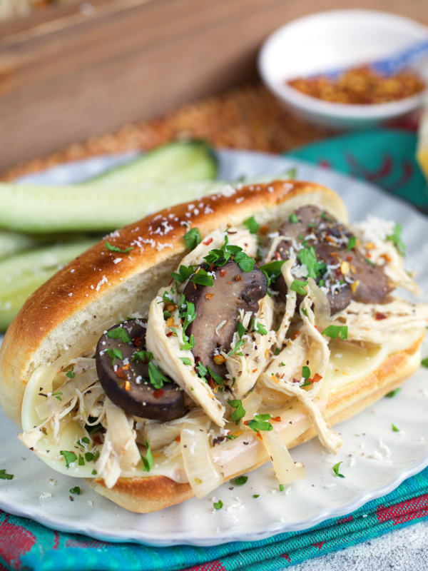 Chicken Cheesesteak Sandwich on a white plate topped with mushrooms.
