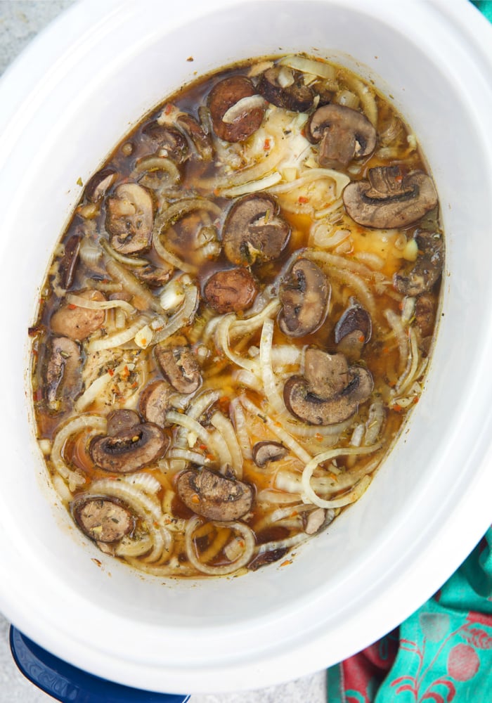 cooked chicken breast with mushrooms and onions in a crock pot