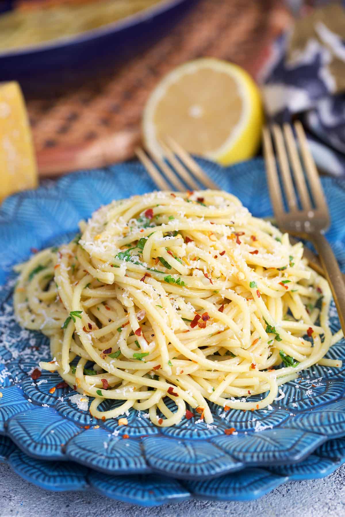 Spaghetti aglio e olio plated on a blue plate with a gold fork and topped with cheese.