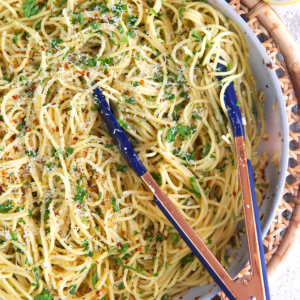 spaghetti aglio e olio in a skillet with tongs.