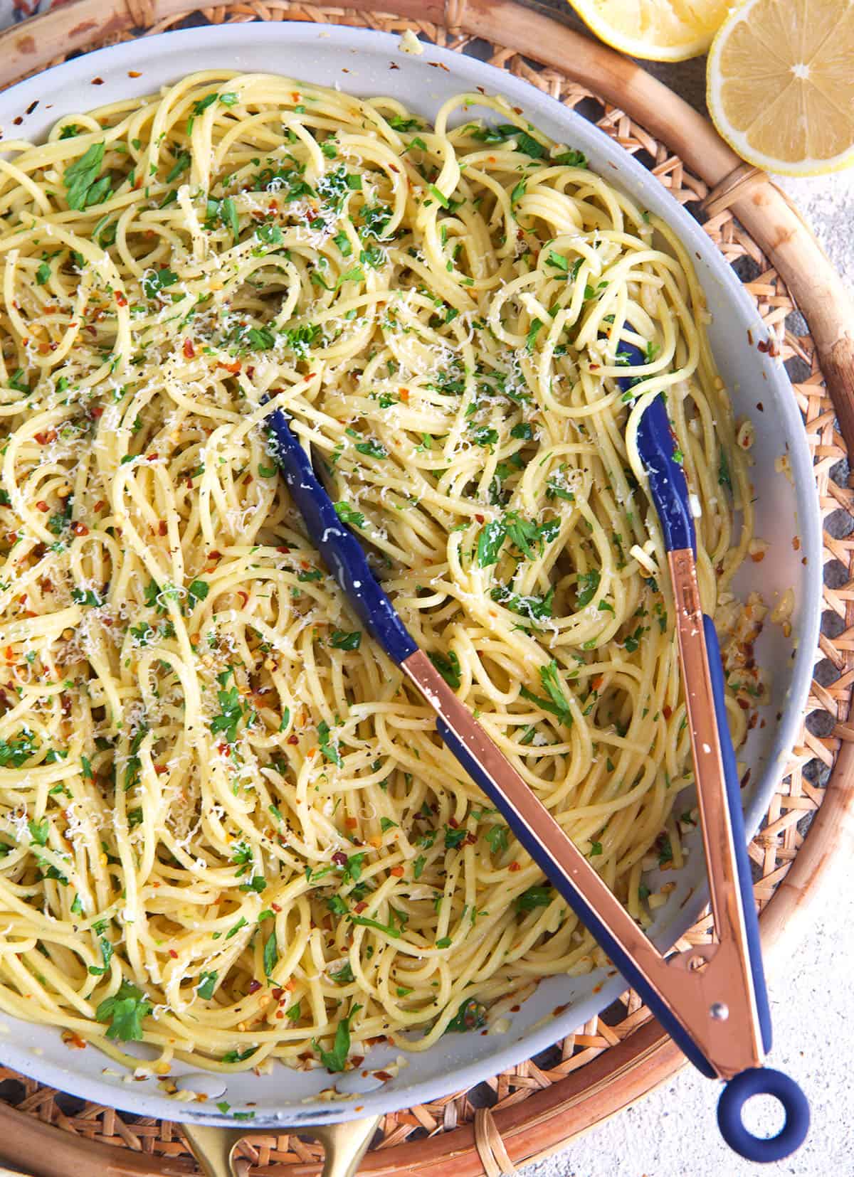 spaghetti aglio e olio in a skillet with tongs.