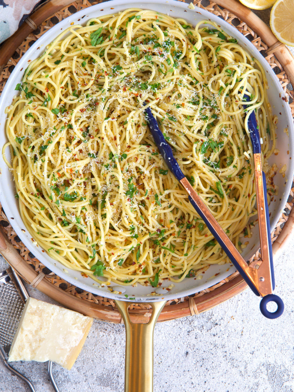 pasta aglio e olio in a skillet with tongs after being cooked.